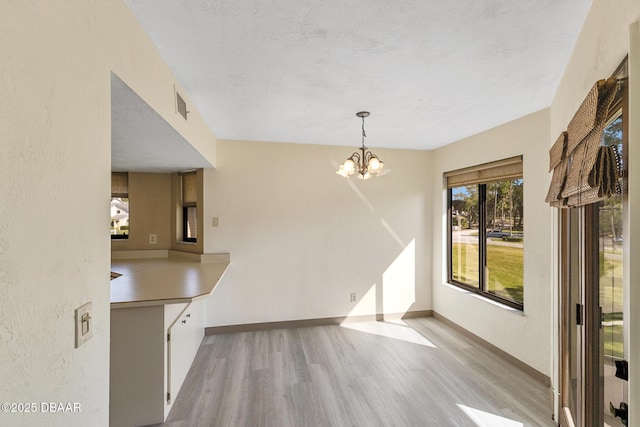 unfurnished dining area with an inviting chandelier, a textured ceiling, and light wood-type flooring