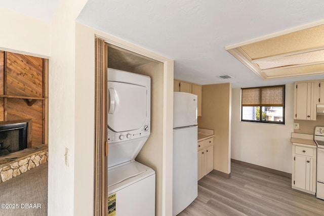 laundry area featuring a stone fireplace, stacked washer and clothes dryer, and light wood-type flooring