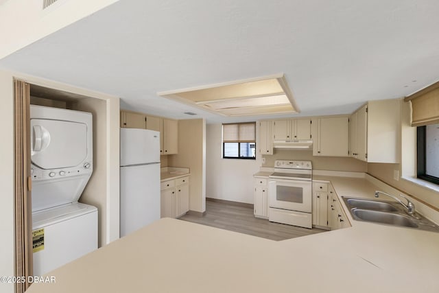 kitchen featuring sink, light wood-type flooring, white appliances, stacked washer / dryer, and cream cabinets