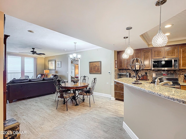 kitchen featuring light stone countertops, hanging light fixtures, stainless steel appliances, decorative backsplash, and ceiling fan with notable chandelier