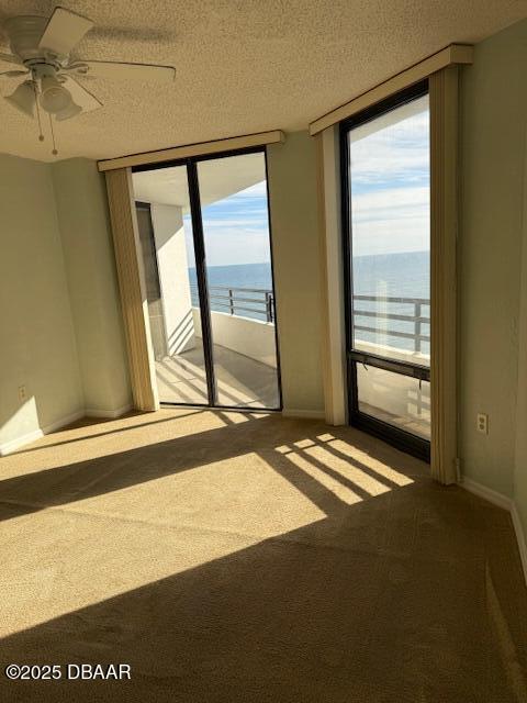 unfurnished room with a textured ceiling, ceiling fan, a healthy amount of sunlight, and a water view