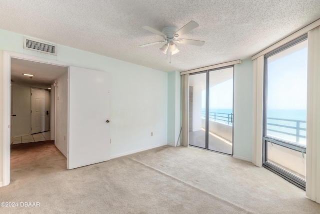 carpeted spare room with a water view, a healthy amount of sunlight, ceiling fan, and a textured ceiling