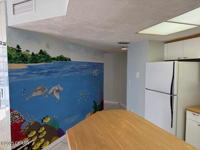 kitchen featuring white fridge, light tile patterned floors, white cabinetry, and a textured ceiling