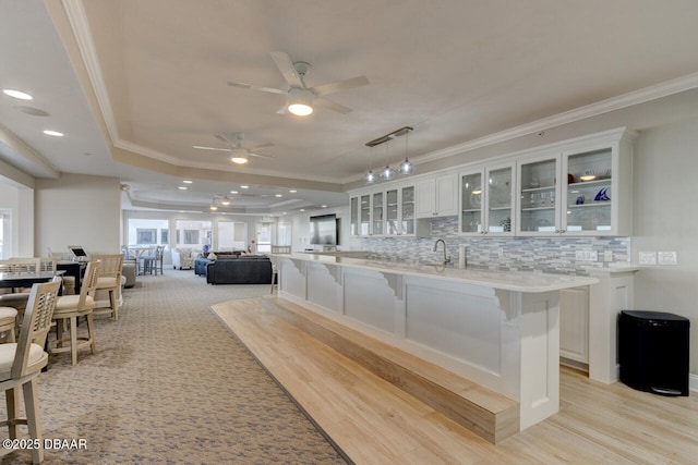 interior space featuring a kitchen bar, crown molding, hanging light fixtures, a raised ceiling, and white cabinets