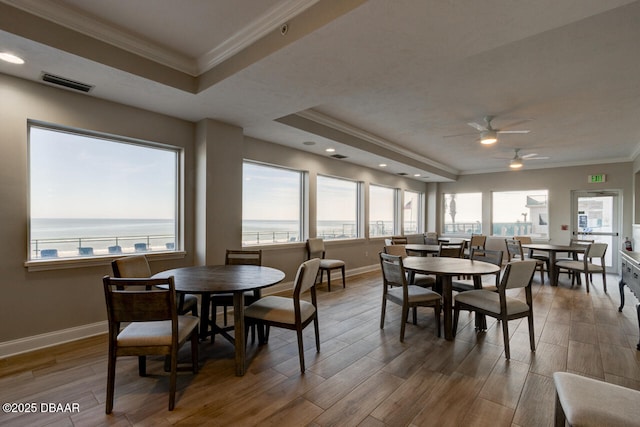 dining space featuring crown molding, a tray ceiling, hardwood / wood-style flooring, and a water view