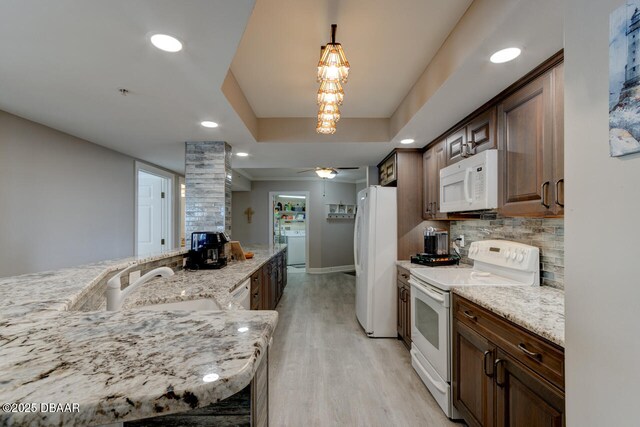 kitchen with light stone counters, light hardwood / wood-style flooring, a tray ceiling, white appliances, and decorative backsplash