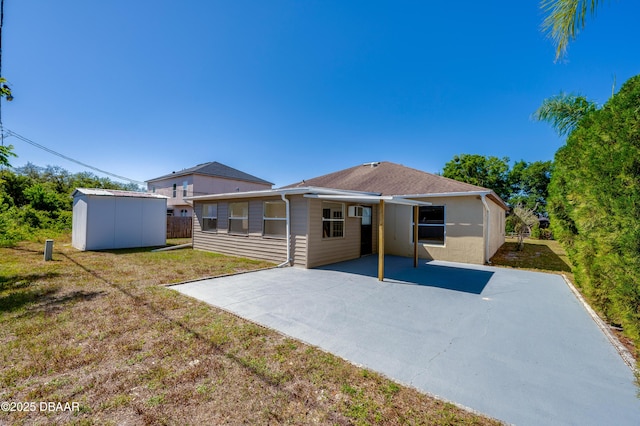 back of house featuring driveway, a patio, a storage unit, an outbuilding, and a lawn