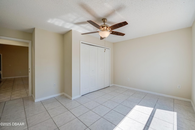 unfurnished bedroom with a closet, baseboards, a ceiling fan, a textured ceiling, and light tile patterned flooring