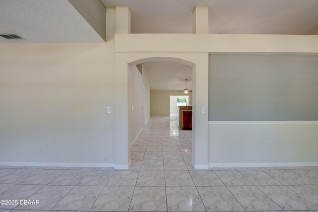 empty room with visible vents, ceiling fan, baseboards, and arched walkways