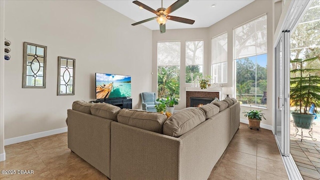 living area featuring a ceiling fan, a lit fireplace, baseboards, and light tile patterned floors