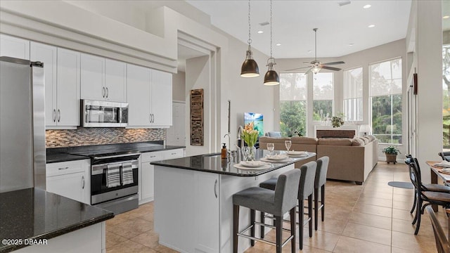 kitchen featuring light tile patterned floors, white cabinetry, open floor plan, appliances with stainless steel finishes, and decorative backsplash