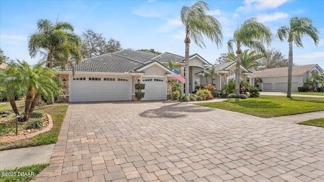 view of front of property featuring an attached garage, a tile roof, decorative driveway, stucco siding, and a front yard