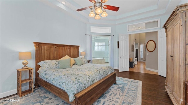 bedroom featuring a tray ceiling, connected bathroom, ceiling fan, wood finished floors, and baseboards