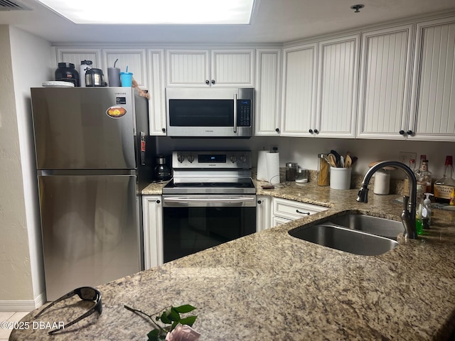 kitchen with visible vents, light stone counters, stainless steel appliances, white cabinetry, and a sink