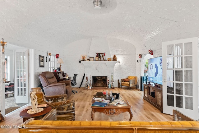 living room with french doors, light hardwood / wood-style floors, a textured ceiling, ceiling fan, and a fireplace