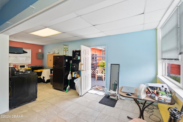 interior space featuring light tile patterned flooring, a paneled ceiling, black appliances, and exhaust hood