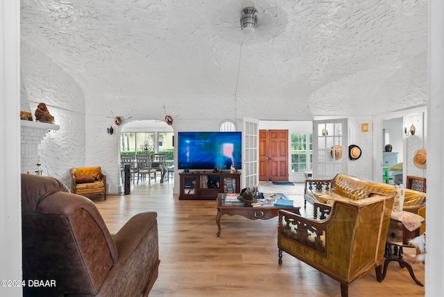 living room featuring light wood-type flooring, a fireplace, lofted ceiling, and a textured ceiling