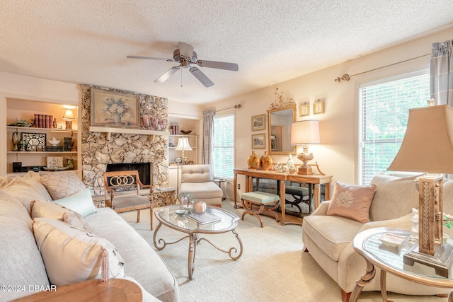 living room featuring ceiling fan, a textured ceiling, a stone fireplace, and carpet floors