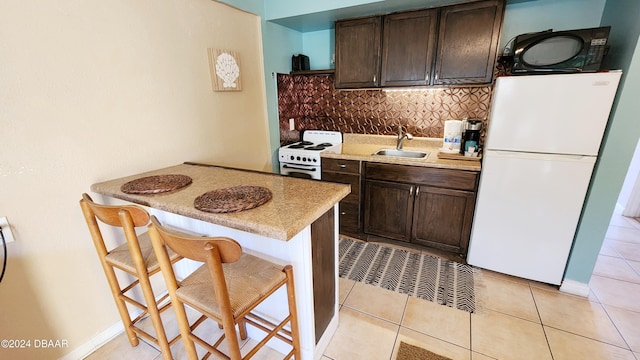 kitchen featuring a kitchen breakfast bar, light tile patterned floors, backsplash, white appliances, and dark brown cabinets