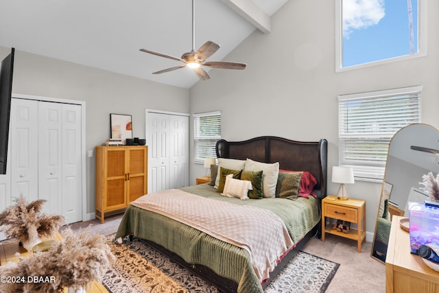 carpeted bedroom featuring high vaulted ceiling, beamed ceiling, ceiling fan, and multiple closets