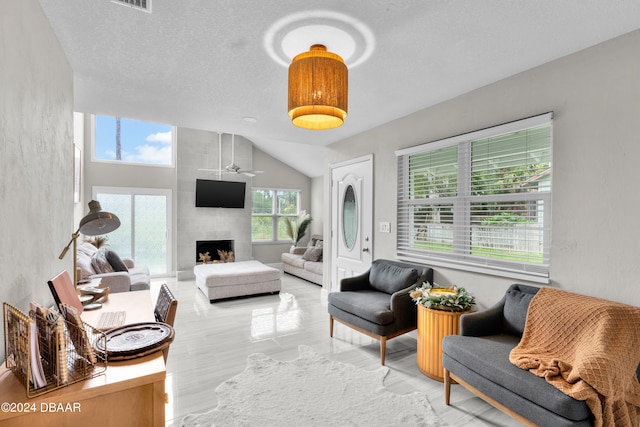 living room with lofted ceiling, a textured ceiling, a tile fireplace, and ceiling fan