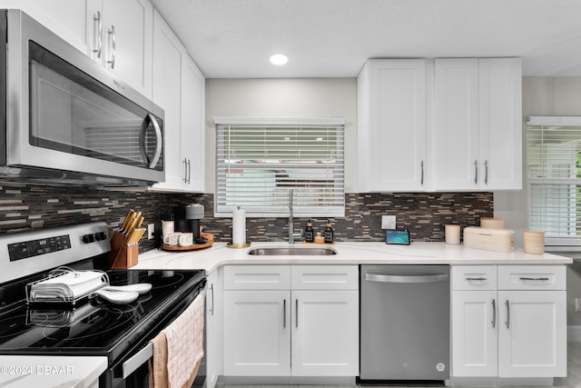 kitchen with a wealth of natural light, appliances with stainless steel finishes, decorative backsplash, and white cabinets