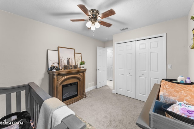 bedroom featuring a textured ceiling, light colored carpet, ceiling fan, and a closet