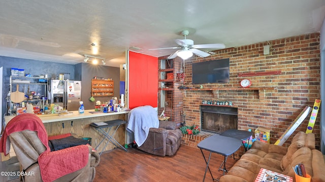 living area with wood finished floors, a ceiling fan, a brick fireplace, and brick wall