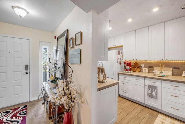 456 Bouchelle Dr Unit 104, New Smyrna Beach, FL 32169 - kitchen featuring wood finish floors, tasteful backsplash, white cabinetry, freestanding refrigerator, and light countertops