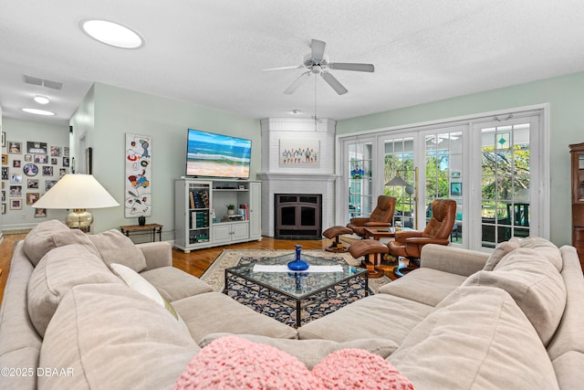 living area featuring visible vents, a fireplace, wood finished floors, a textured ceiling, and a ceiling fan