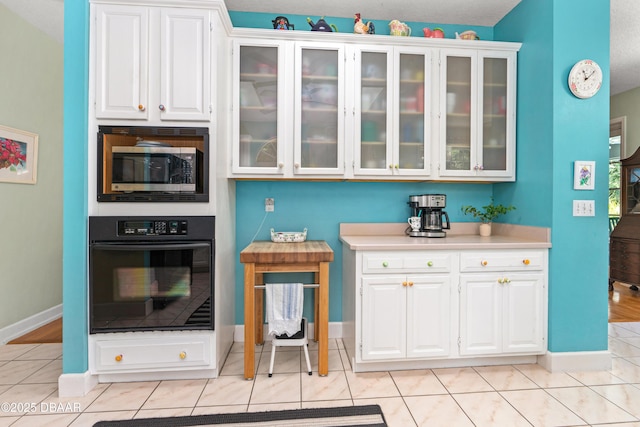 kitchen featuring stainless steel microwave, black oven, glass insert cabinets, and white cabinets