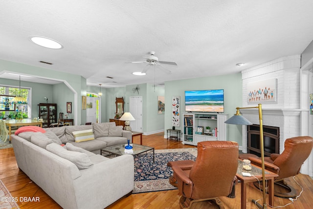 living room featuring visible vents, a brick fireplace, ceiling fan with notable chandelier, wood finished floors, and a textured ceiling