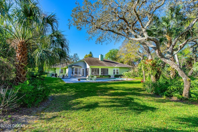 rear view of house with an outdoor pool, stucco siding, a lawn, and a chimney