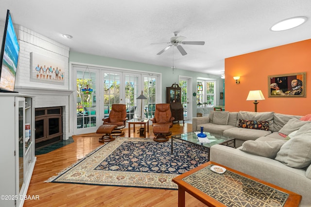 living area with a fireplace, ceiling fan, wood finished floors, and a textured ceiling