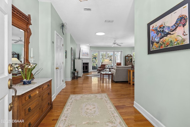 hall featuring visible vents, light wood-style flooring, and baseboards