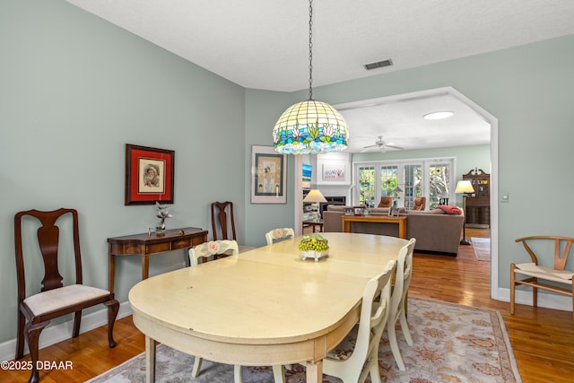 dining space featuring wood finished floors, visible vents, baseboards, a fireplace, and arched walkways