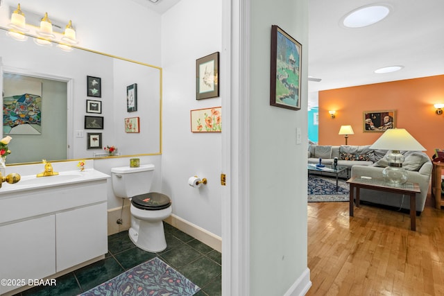 bathroom with toilet, vanity, baseboards, and wood finished floors