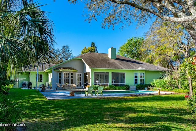 rear view of house with stucco siding, a yard, a chimney, and a patio area