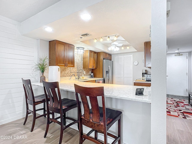 kitchen featuring a raised ceiling, light hardwood / wood-style flooring, kitchen peninsula, stainless steel fridge, and a breakfast bar