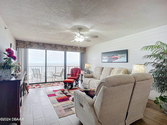 living room with ceiling fan, a water view, a textured ceiling, and light hardwood / wood-style flooring