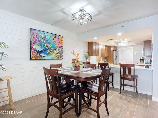 dining space featuring wood walls, light hardwood / wood-style floors, and a textured ceiling