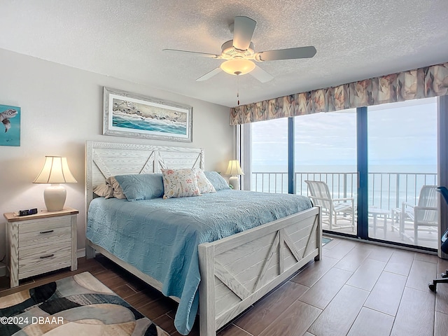 bedroom featuring access to outside, a water view, ceiling fan, dark hardwood / wood-style floors, and a textured ceiling