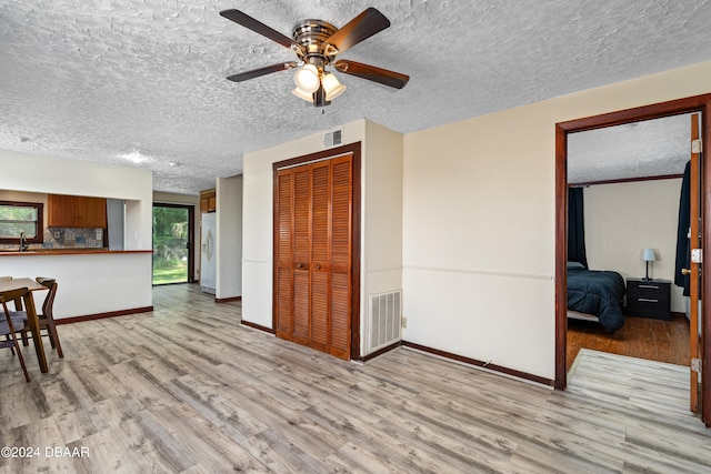 interior space with ceiling fan, a textured ceiling, sink, and light wood-type flooring