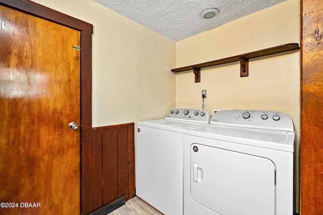 washroom featuring light hardwood / wood-style floors, wooden walls, a textured ceiling, and independent washer and dryer