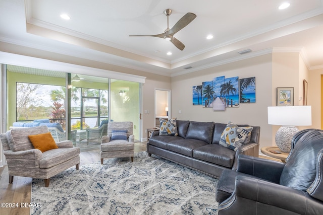 living room with wood-type flooring, a tray ceiling, ceiling fan, and ornamental molding