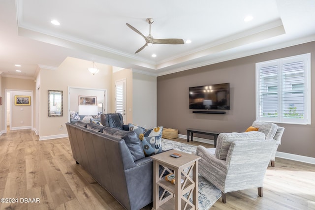 living room with light hardwood / wood-style floors, a raised ceiling, ceiling fan, and ornamental molding