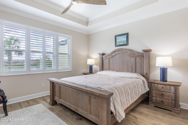 bedroom with a tray ceiling, crown molding, ceiling fan, and light wood-type flooring