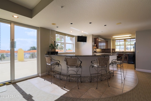 kitchen with black refrigerator, kitchen peninsula, decorative backsplash, light tile patterned floors, and a breakfast bar