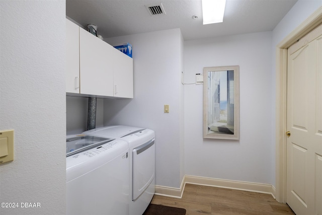 clothes washing area with washing machine and dryer, cabinets, and hardwood / wood-style flooring