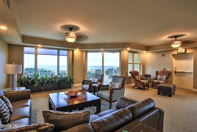 carpeted living room featuring ceiling fan, a textured ceiling, and a water view